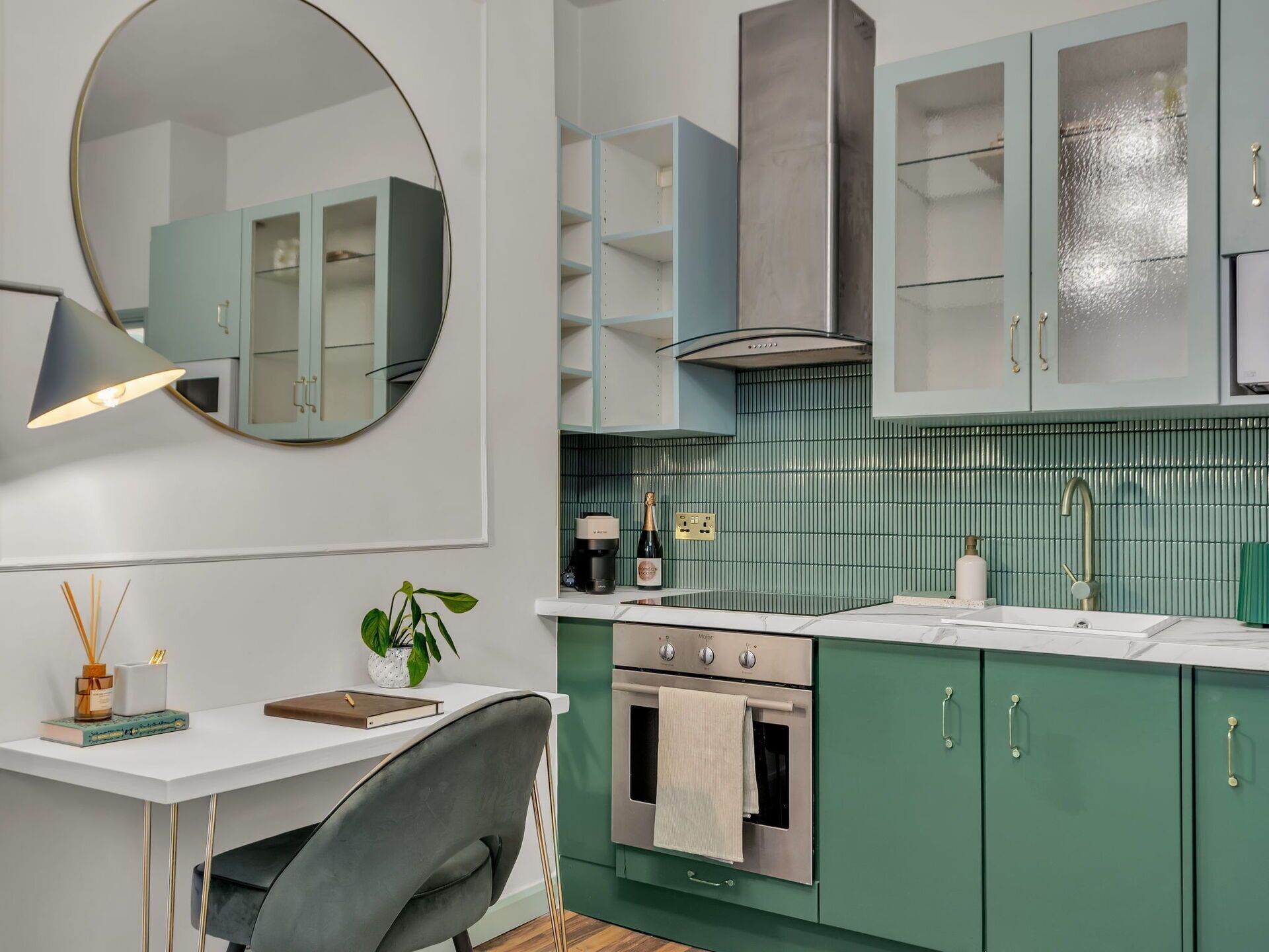 A modern kitchen with green cabinets, a stainless steel oven, a sink, and a round mirror.