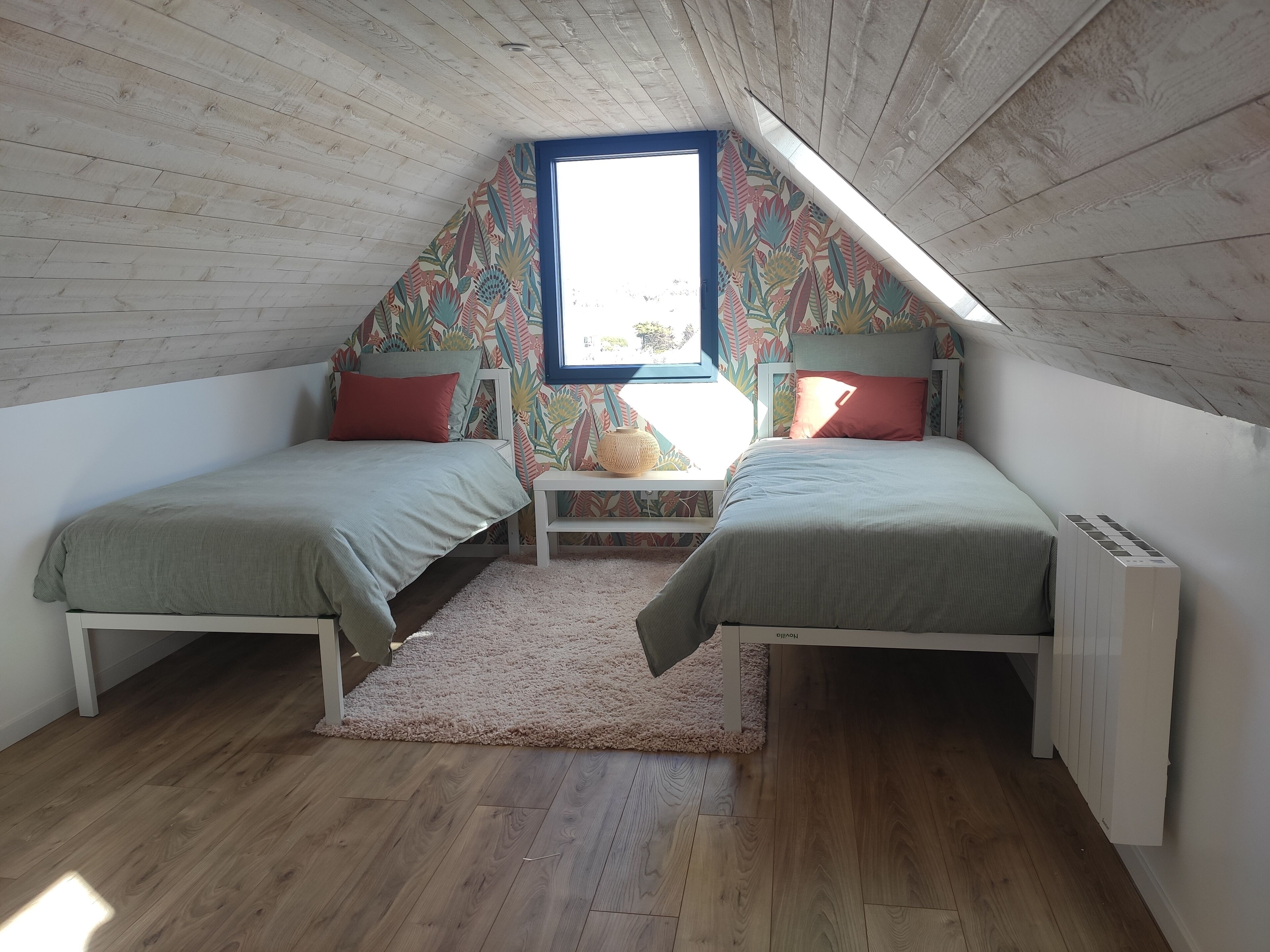 Ein kleines, gemütliches Schlafzimmer im Dachgeschoss mit zwei Einzelbetten, Holzboden, geneigter Decke und einem Fenster mit Blick.