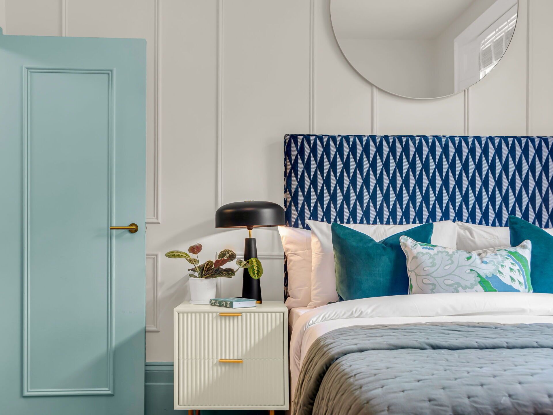 A bedroom with a bed, a nightstand, a lamp, and a potted plant.