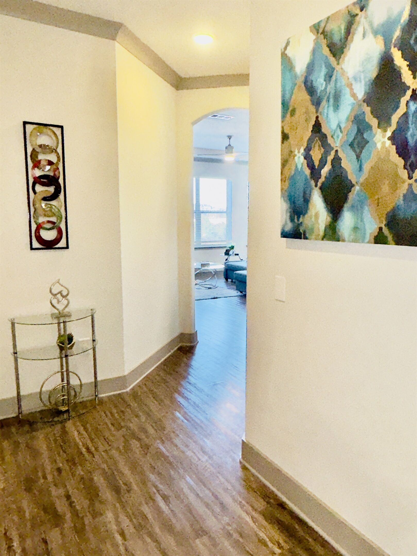 A hallway with wooden flooring, a metal stand with a plant, and a colorful abstract painting on the wall.