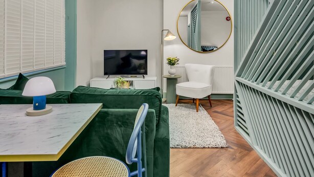 Een moderne woonkamer met een groene bank, een televisie, een witte stoel en een ronde spiegel.