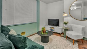 Een moderne woonkamer met een groene bank, een ronde salontafel, een flatscreen televisie, een spiegel en een lamp.