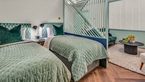 Een moderne slaapkamer met twee bedden, een trap, een klein tafeltje met een plant en een raam met jaloezieën.