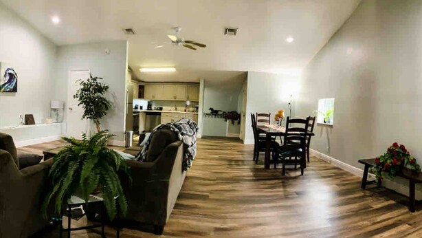 Ampla sala de estar com piso de madeira, um sofá, uma mesa de jantar com cadeiras e um ventilador de teto.