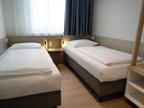 Une chambre double avec deux lits, une table de chevet, une commode, une fenêtre avec des rideaux et un plancher en bois.