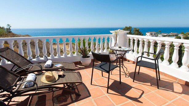 A terrace with wicker lounge chairs, a small table, and a potted plant, overlooking a coastal view. - Beautiful apartment for 4 guests with WIFI, pool, A/C, TV, terrace and pets allowed (Torrox)