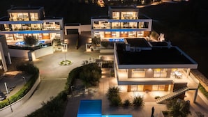 Une maison moderne à plusieurs étages, dotée d’une piscine centrale, de nombreux balcons et d’une allée bien éclairée.