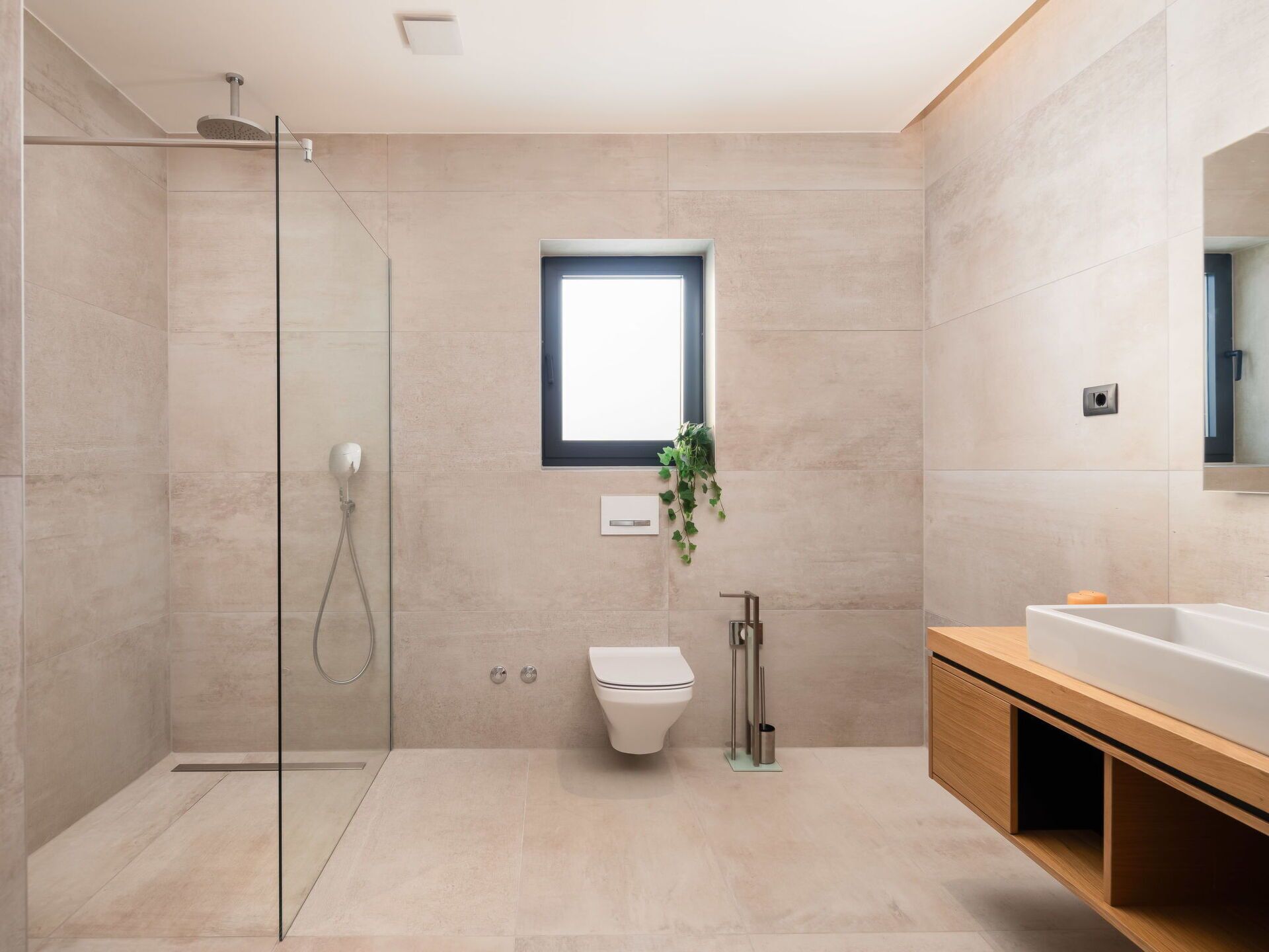 A modern bathroom with a glass shower enclosure, a toilet, a sink with a wooden vanity, and a window providing natural light.