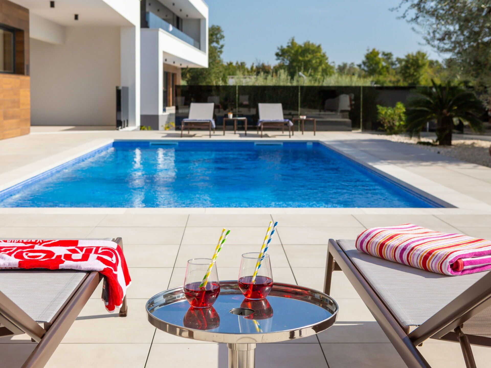Un área de piscina moderna al aire libre con sillones de descanso y una mesa con bebidas.