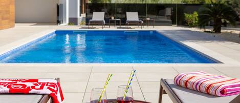 Un área de piscina moderna al aire libre con sillones de descanso y una mesa con bebidas.