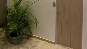 Fachada moderna de um edifício com uma porta de madeira marcada com o número 6, um vaso de planta e três luminárias fixadas na parede.
