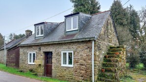 Une maison en pierre avec un toit en pente, une porte en bois et un petit escalier menant à un grenier.