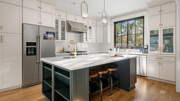 Una cocina moderna con armarios blancos, electrodomésticos de acero inoxidable, una isla grande con taburetes y un amplio ventanal que proporciona luz natural.