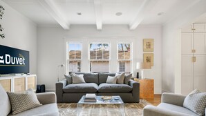 Una sala de estar con un sofá gris, dos sillones, una mesa de centro y un televisor sobre un mueble.