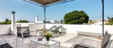A rooftop terrace with outdoor furniture, a pergola, and a view of the cityscape.
