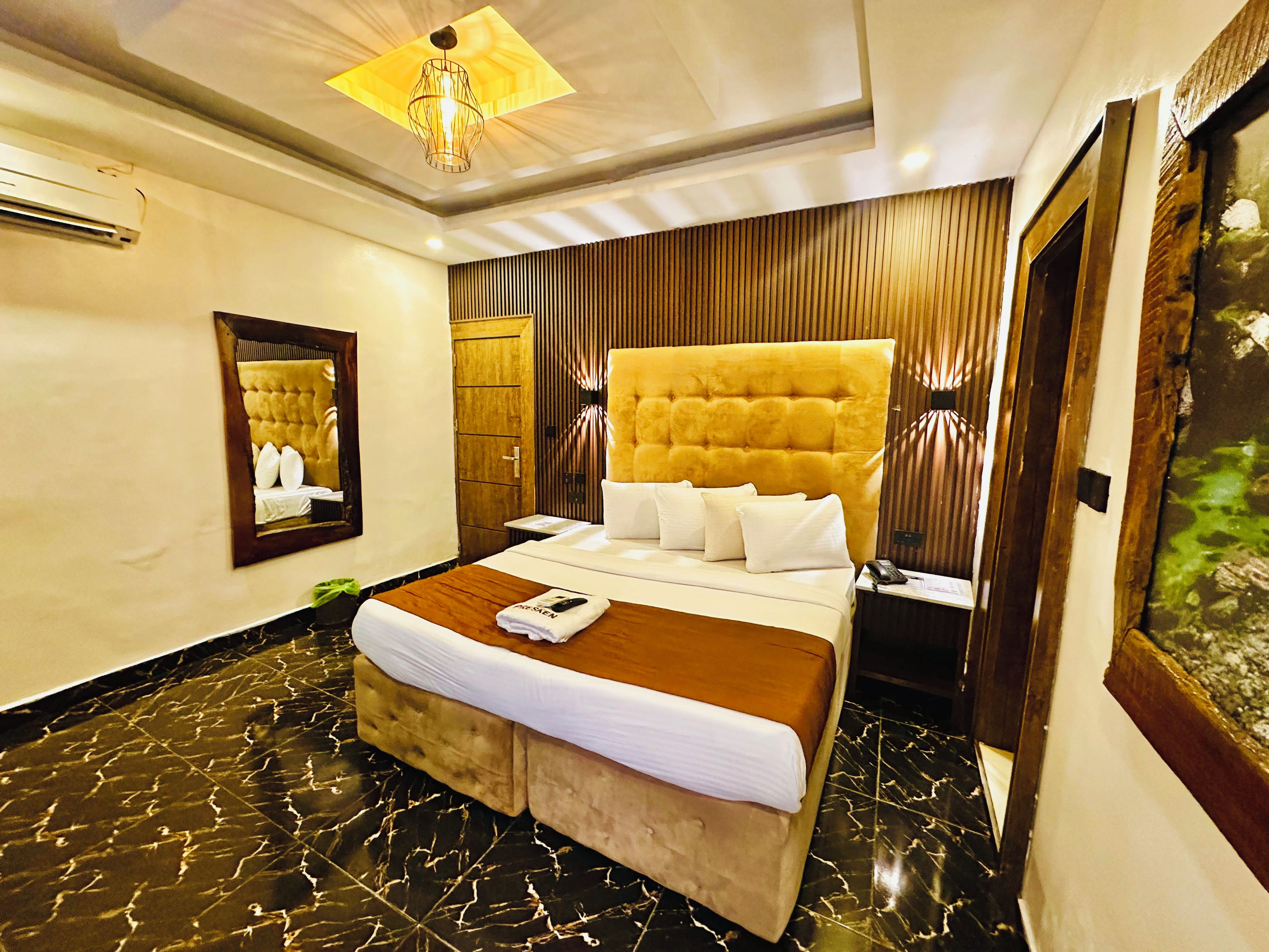 A hotel room with a large bed, a wooden headboard, a mirror, and a ceiling light fixture.