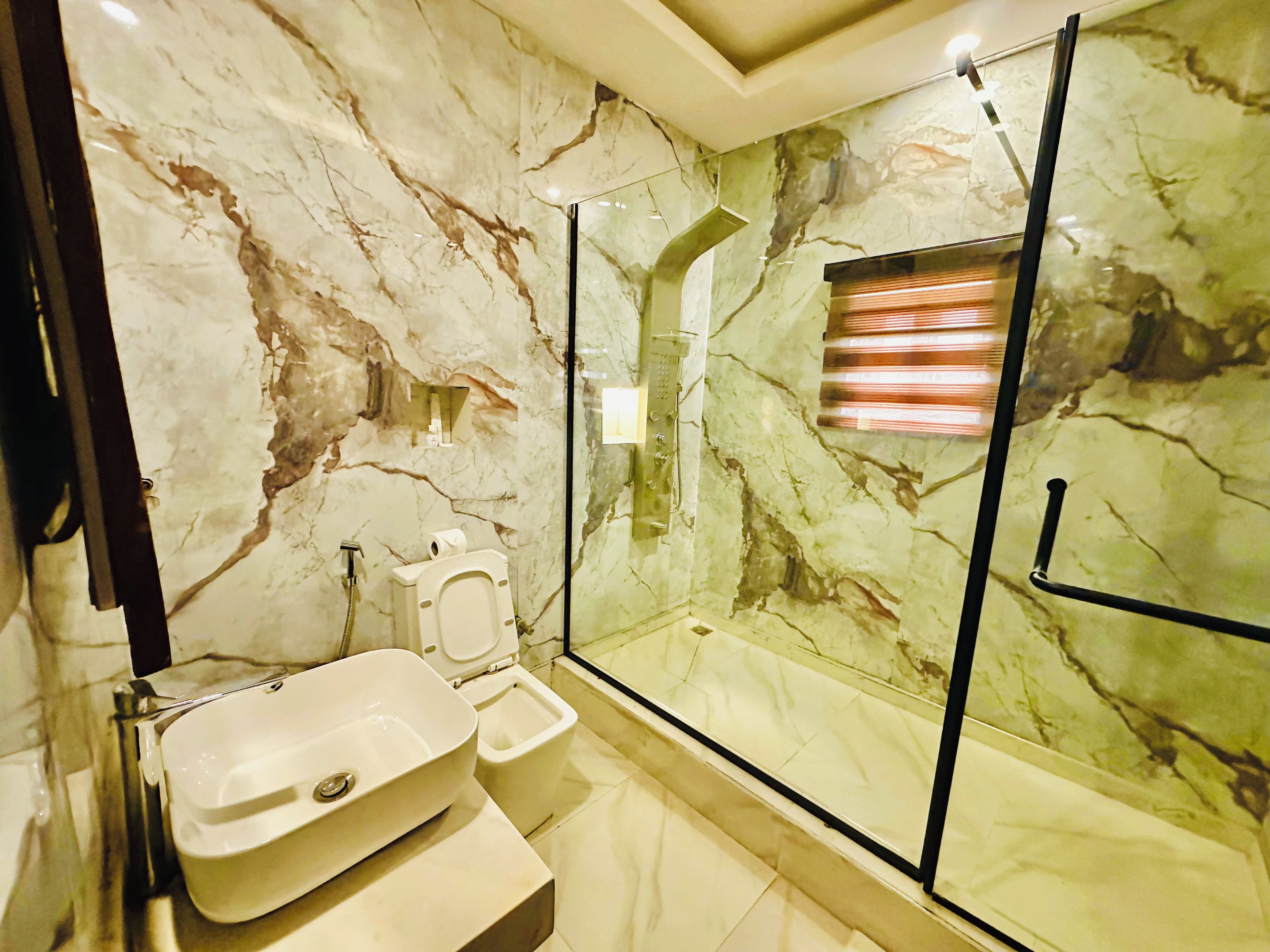 A bathroom with a marble wall, a glass shower enclosure, a sink, and a toilet.