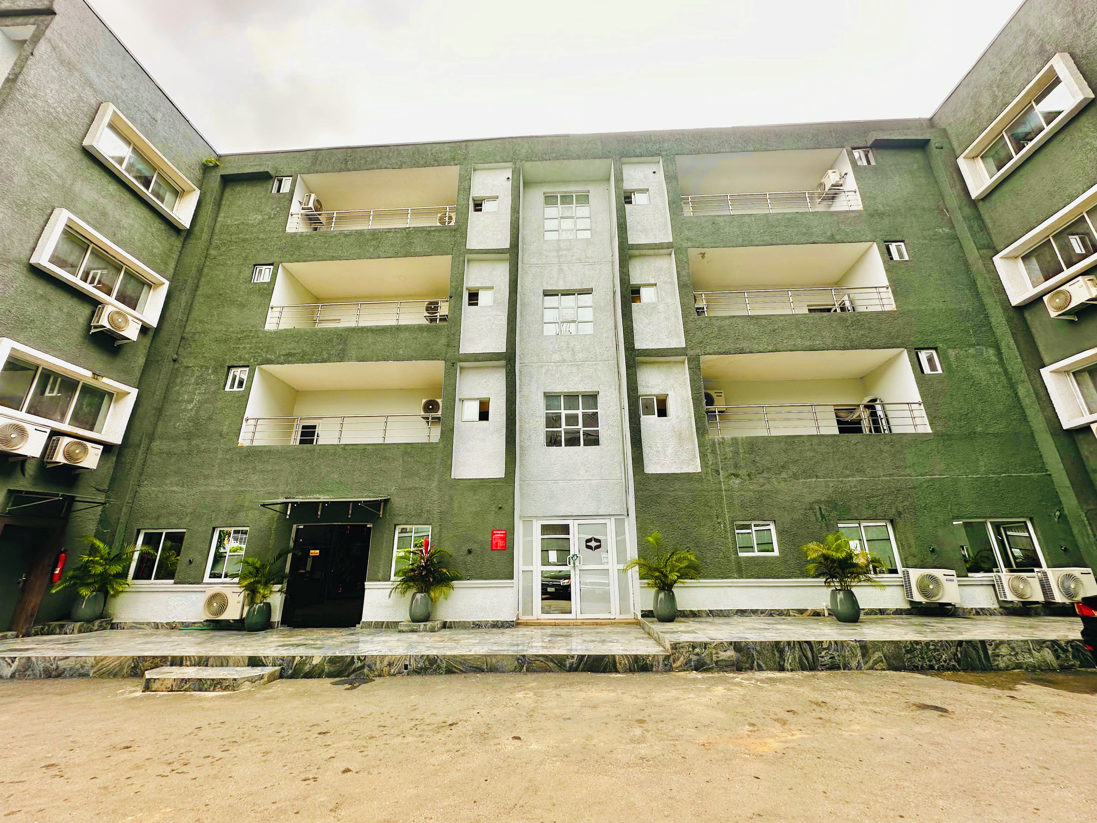 A multi-story building with balconies, air conditioning units, and a central entrance.