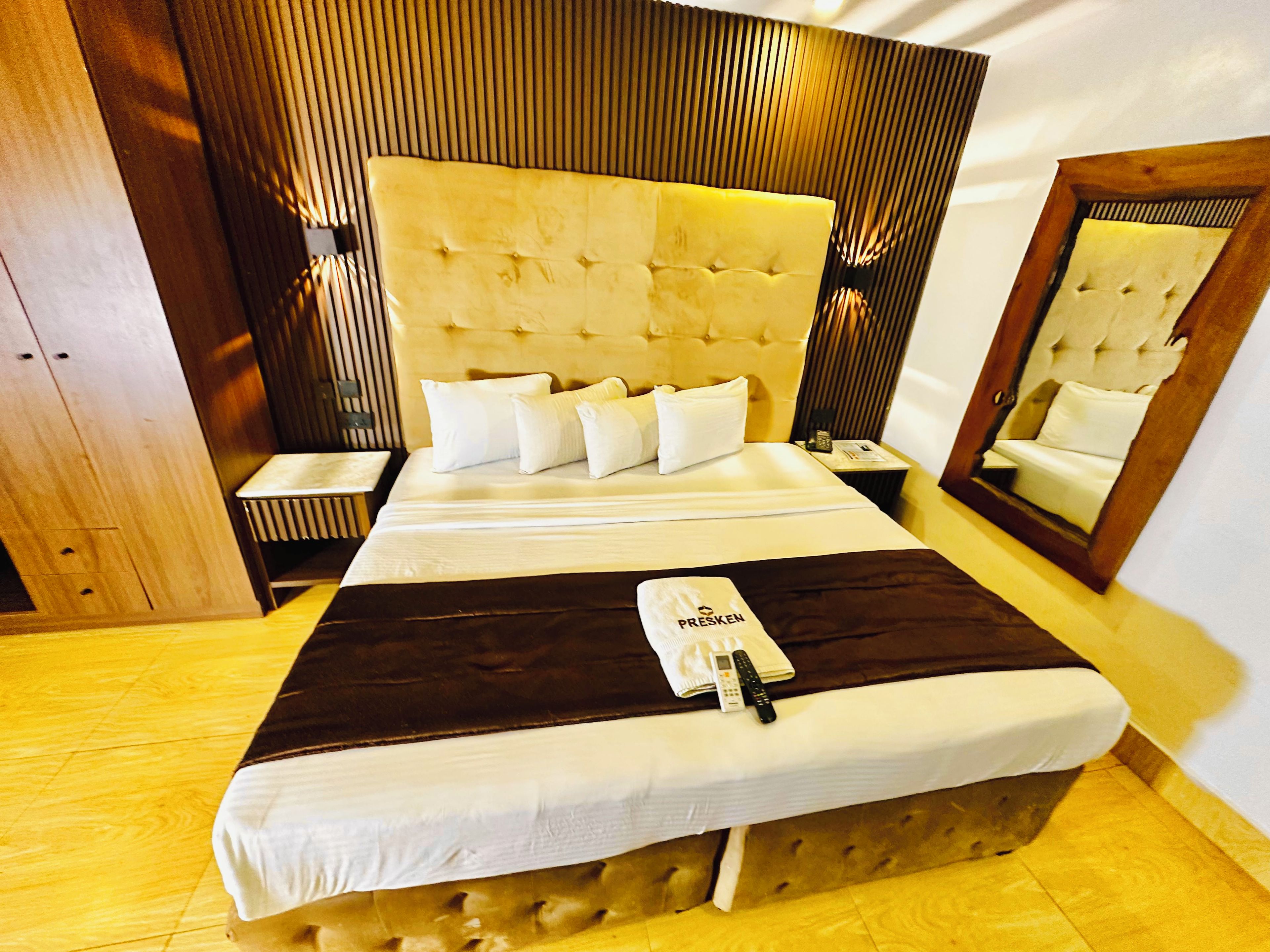 A hotel room with a large bed, a bedside table, a mirror, and a wooden headboard.