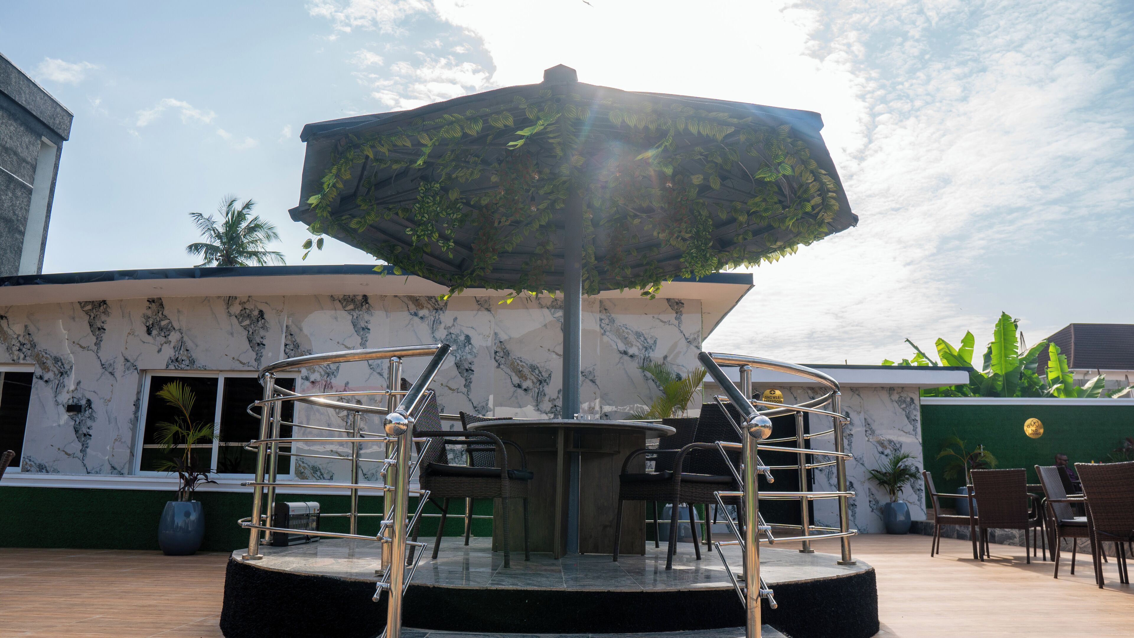 A covered outdoor seating area with a central table and chairs, surrounded by a building with a marble facade.