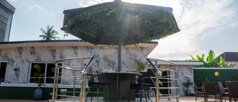 A covered outdoor seating area with a central table and chairs, surrounded by a building with a marble facade.