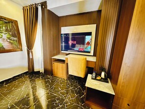 A hotel room with a flat-screen TV mounted on the wall, a wooden desk, a cushioned chair, and a marble-patterned floor. - Presken Hotel Residence  (Lagos)