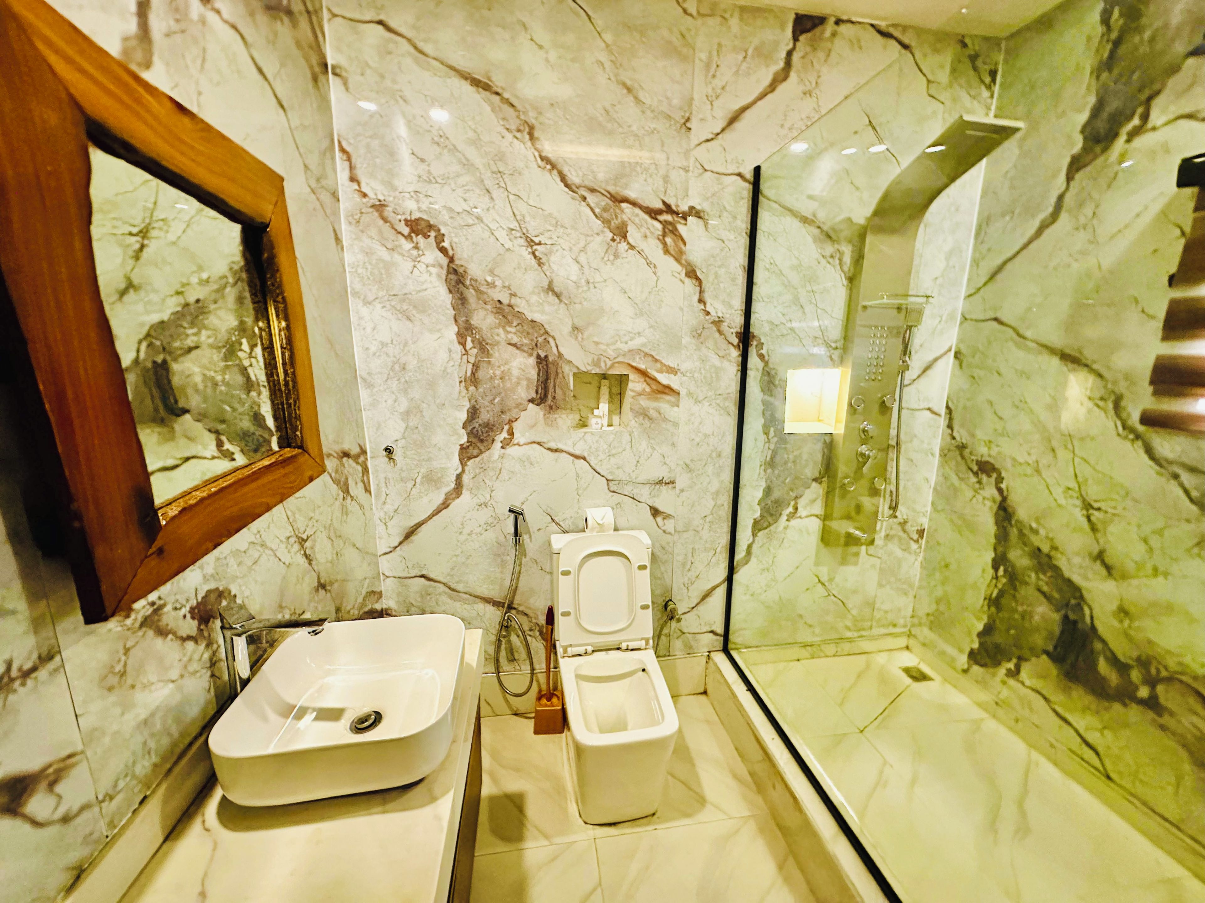 Un baño con pared de mármol, un lavamanos, un inodoro y una zona de ducha con mampara de vidrio.