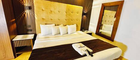 A hotel room with a large bed, a bedside table, a nightstand, a mirror, and a wooden headboard.