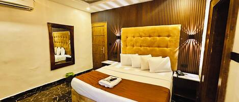 A hotel room with a large bed, a wooden headboard, a mirror, a bedside table, and a modern light fixture.