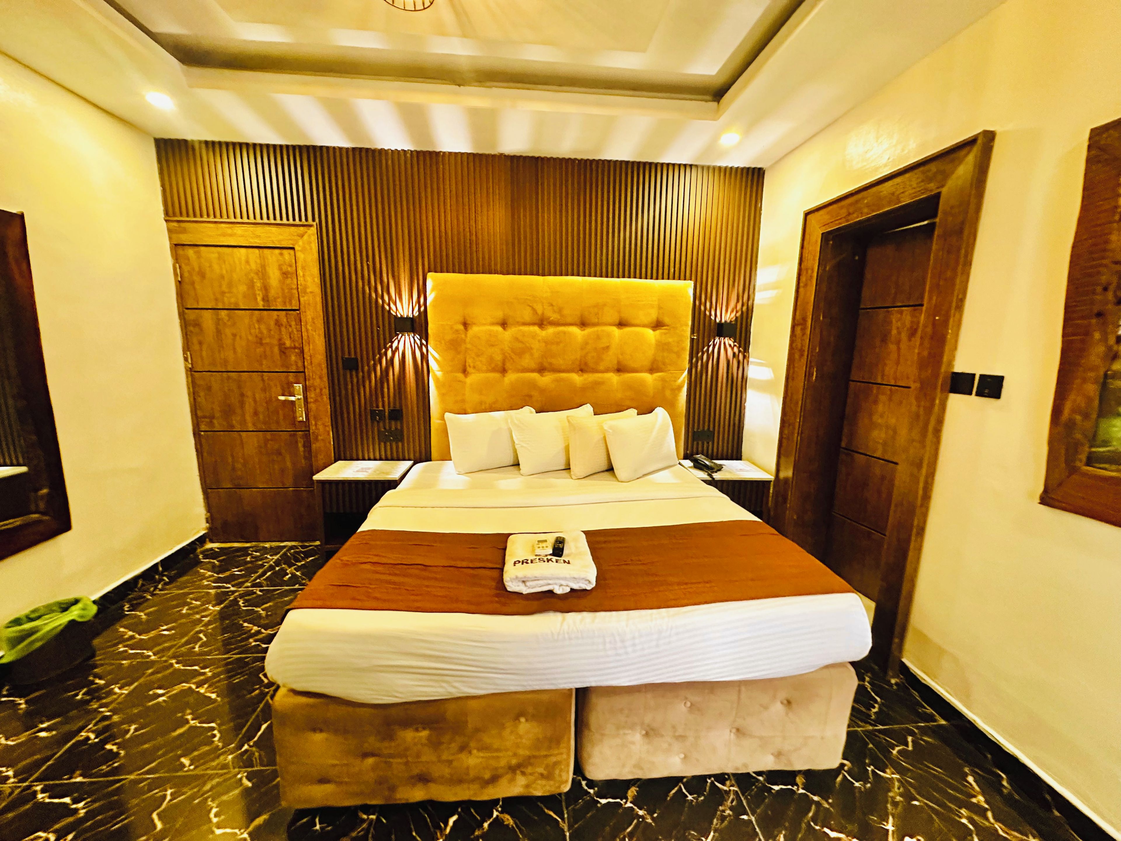 A hotel room with a large bed, wooden paneling, a marble floor, and a wooden door.
