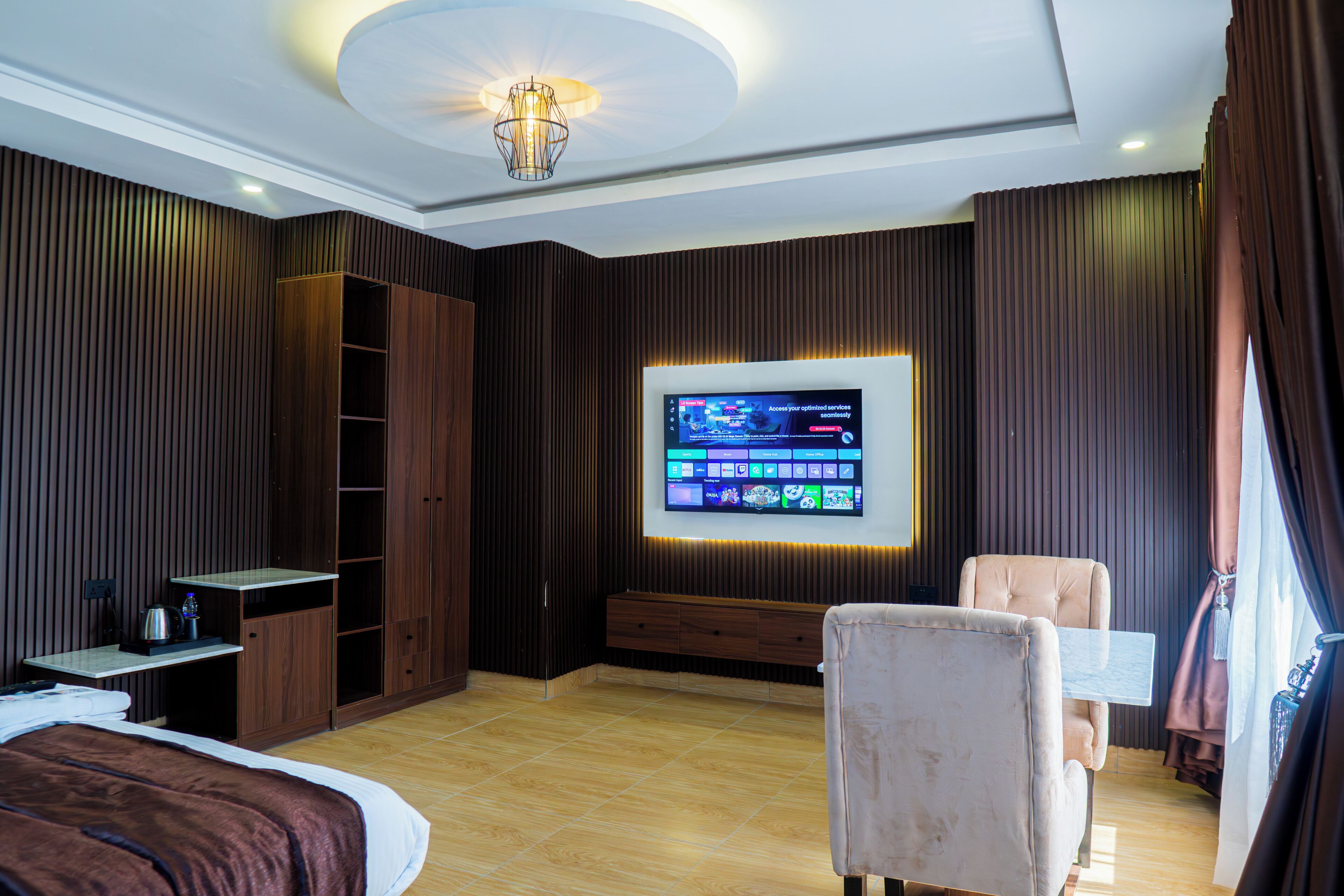 A hotel room with a bed, a seating area, a TV mounted on the wall, and a wardrobe.