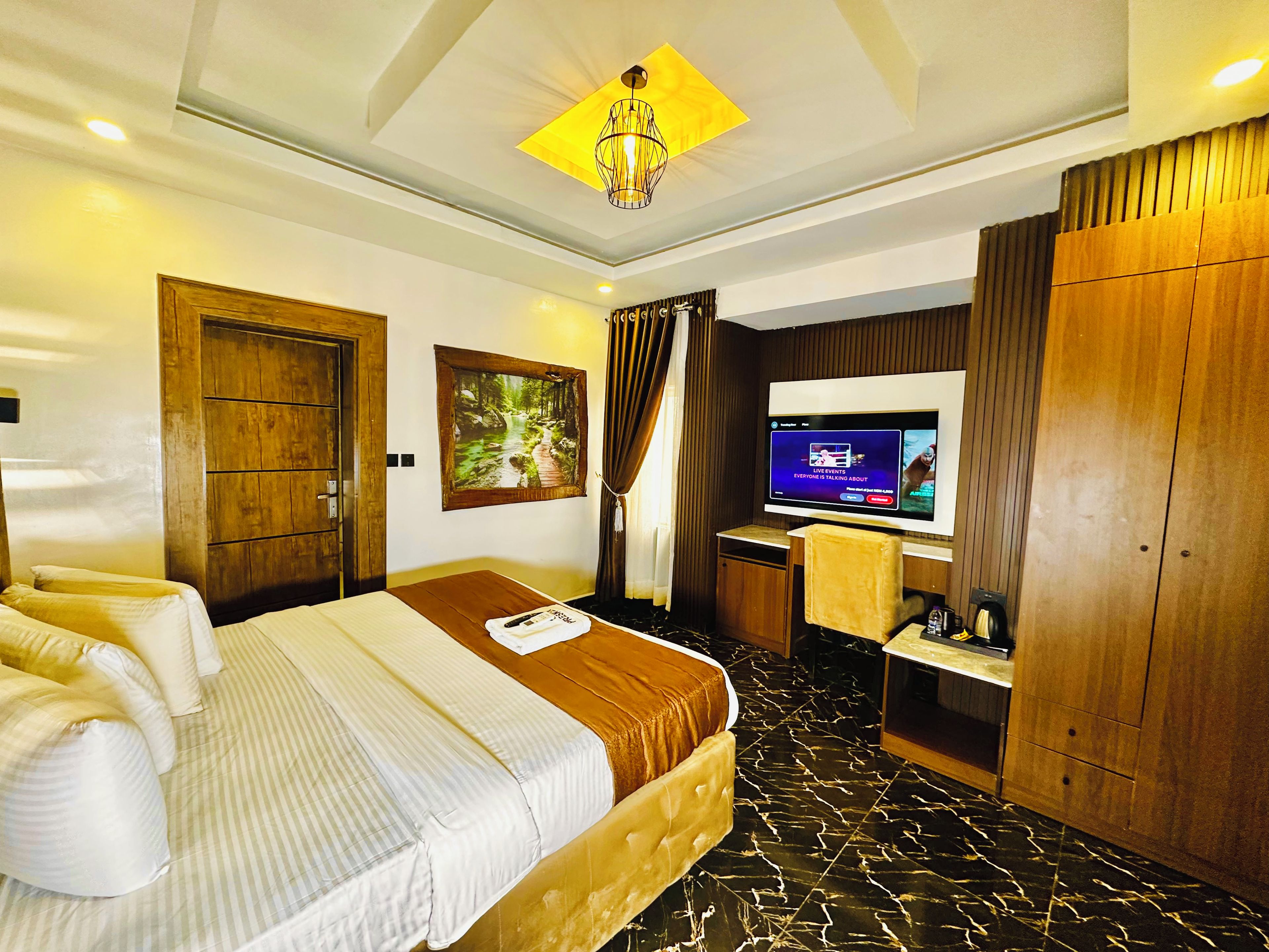 Una habitación de hotel con una cama, televisión, armario de madera y un cuadro en la pared.