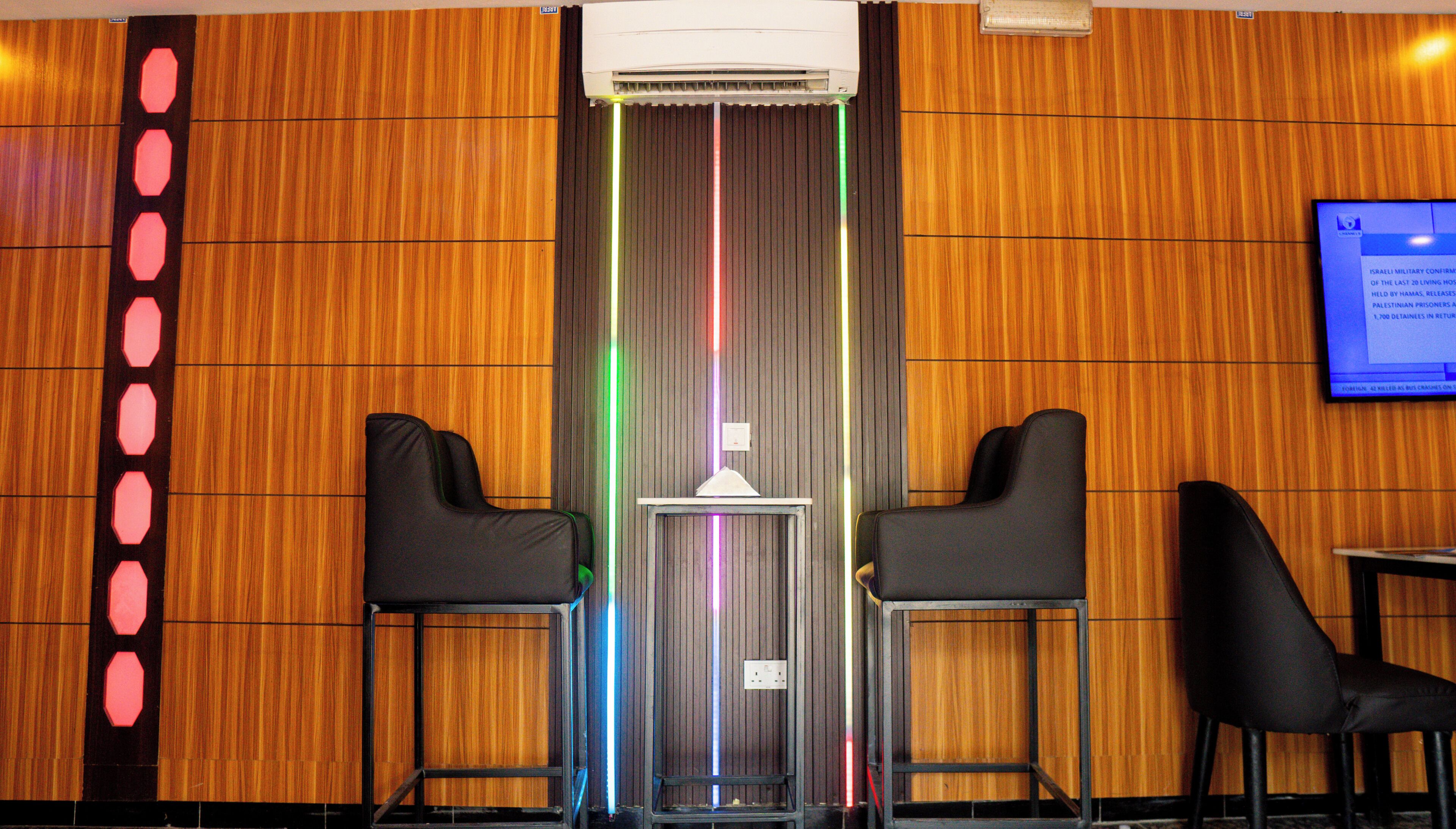 A room with wooden paneling, two black chairs, a small table, and a wall-mounted TV.
