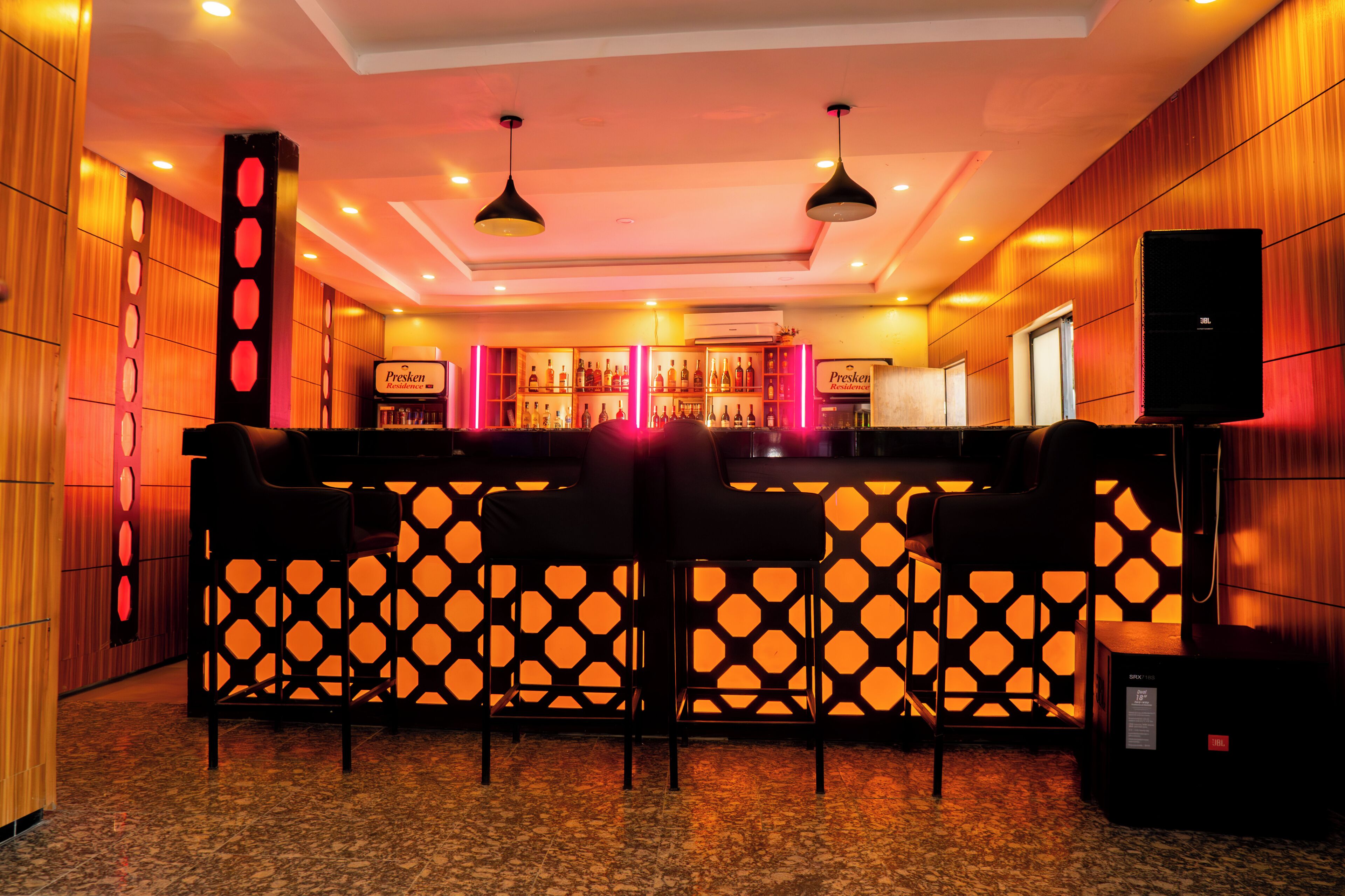 A bar area with a patterned partition, bar stools, and a shelf with bottles.
