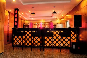 Una zona de bar con un separador decorado, taburetes y una estantería con botellas.