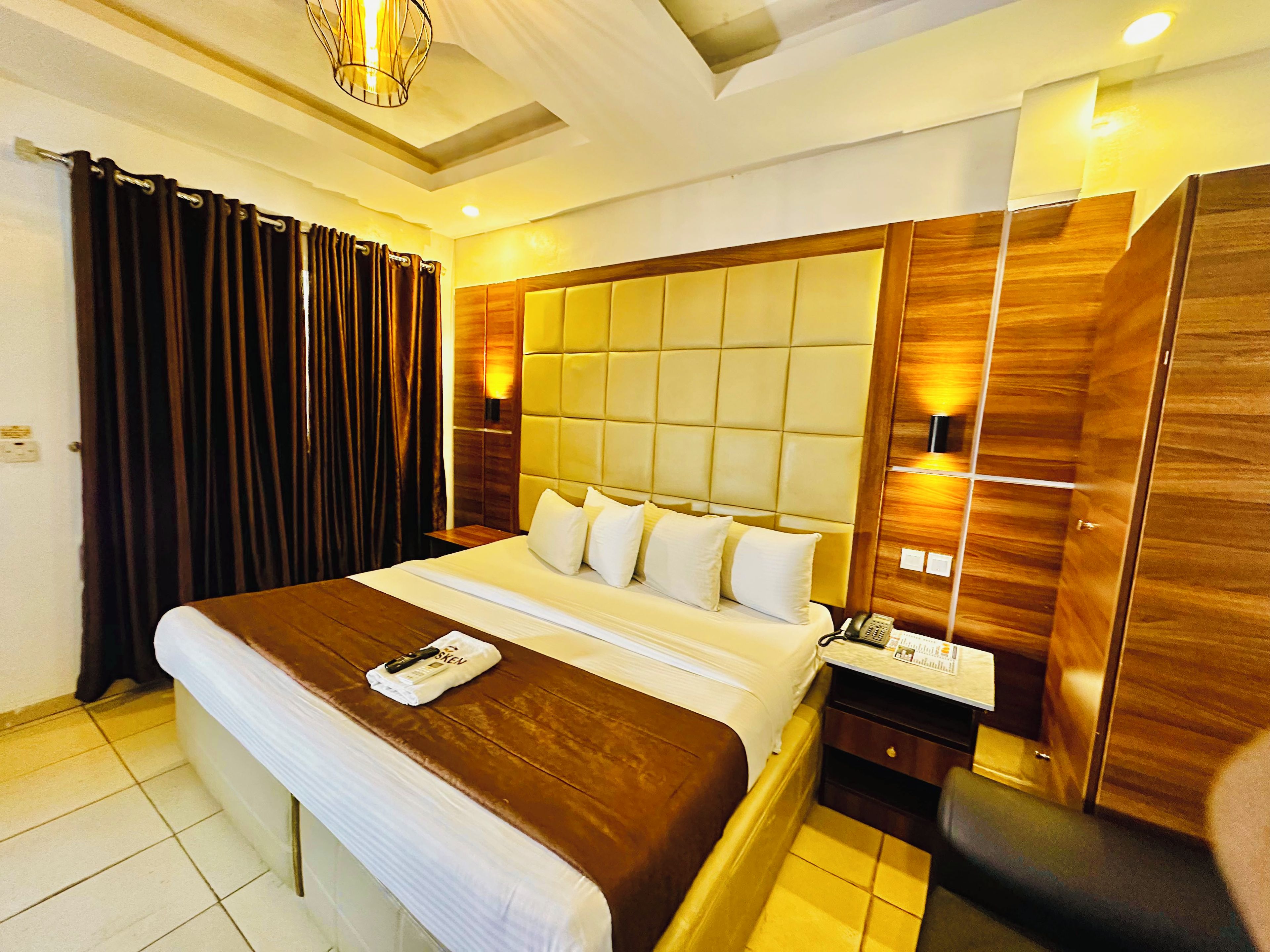 A hotel room with a large bed, wooden headboard, bedside lamps, and a small table with a telephone.