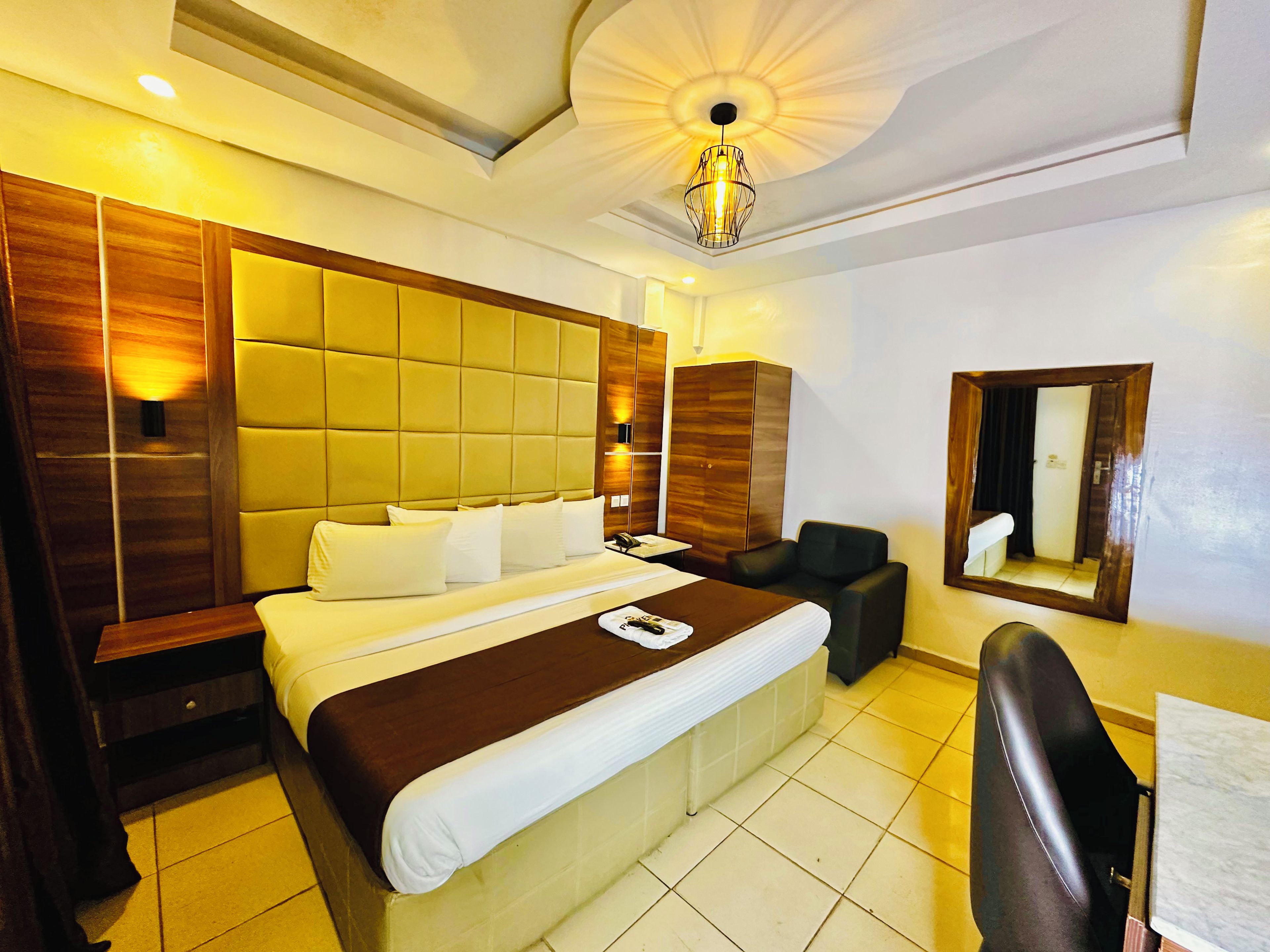 A hotel room with a large bed, a bedside table, a chair, a wardrobe, and a mirror on the wall.