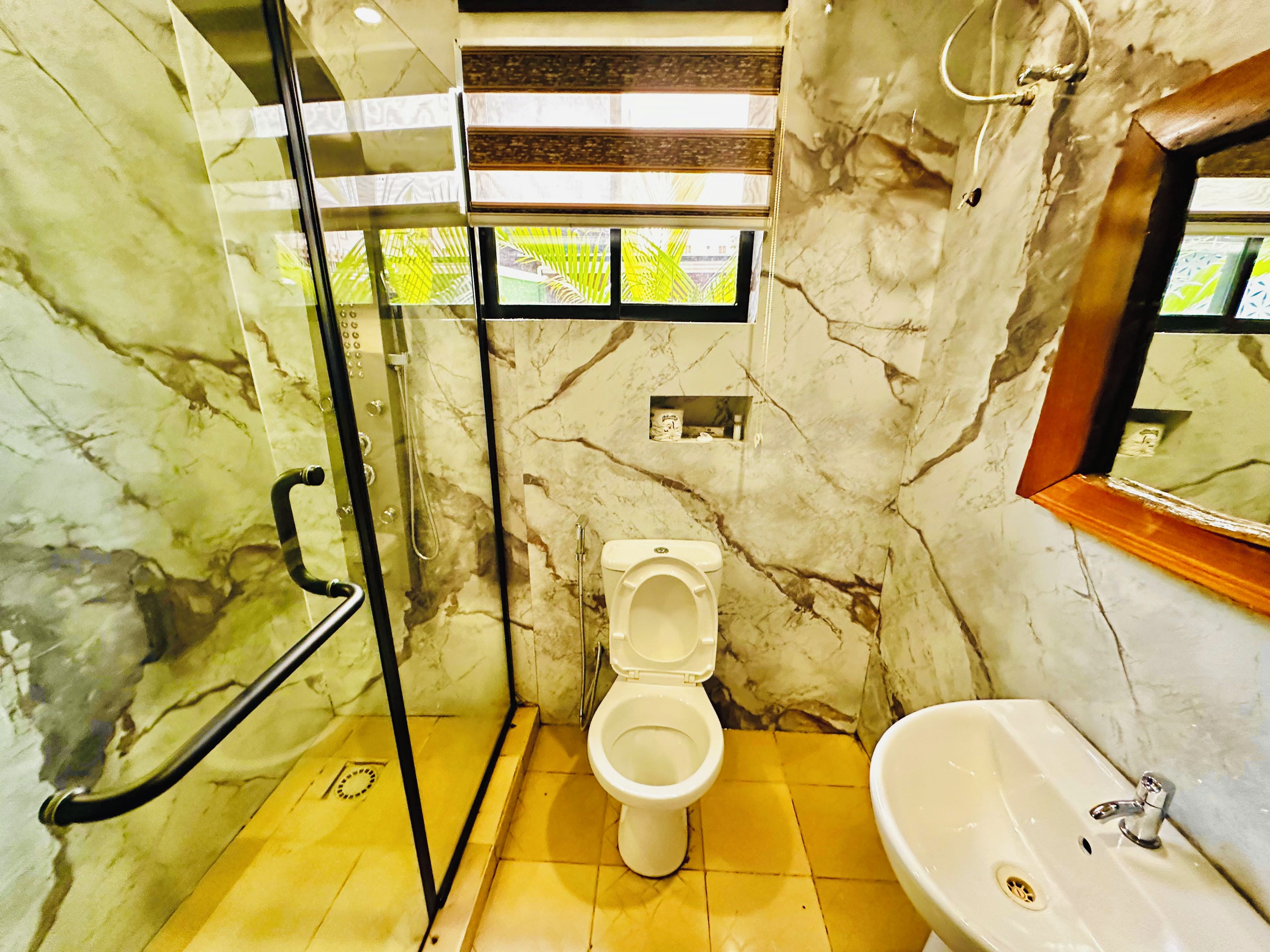 Ein Badezimmer mit Marmorwand, Toilette, Waschbecken und Duschbereich.