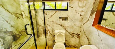 Ein Badezimmer mit Marmorwand, Toilette, Waschbecken und Duschbereich.