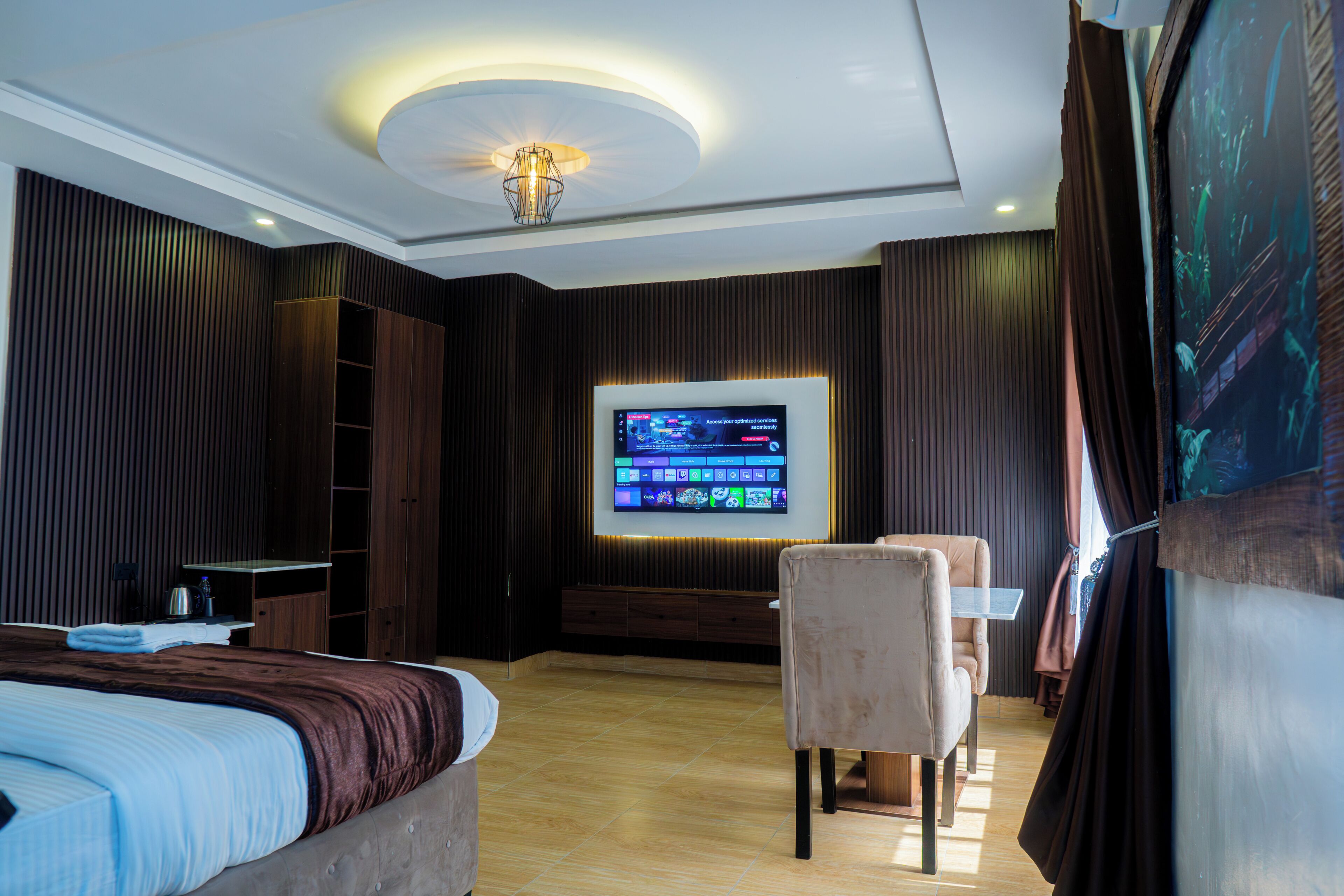 Ett hotellrum med en stor platt-TV, en säng, en stol och ett skrivbord.