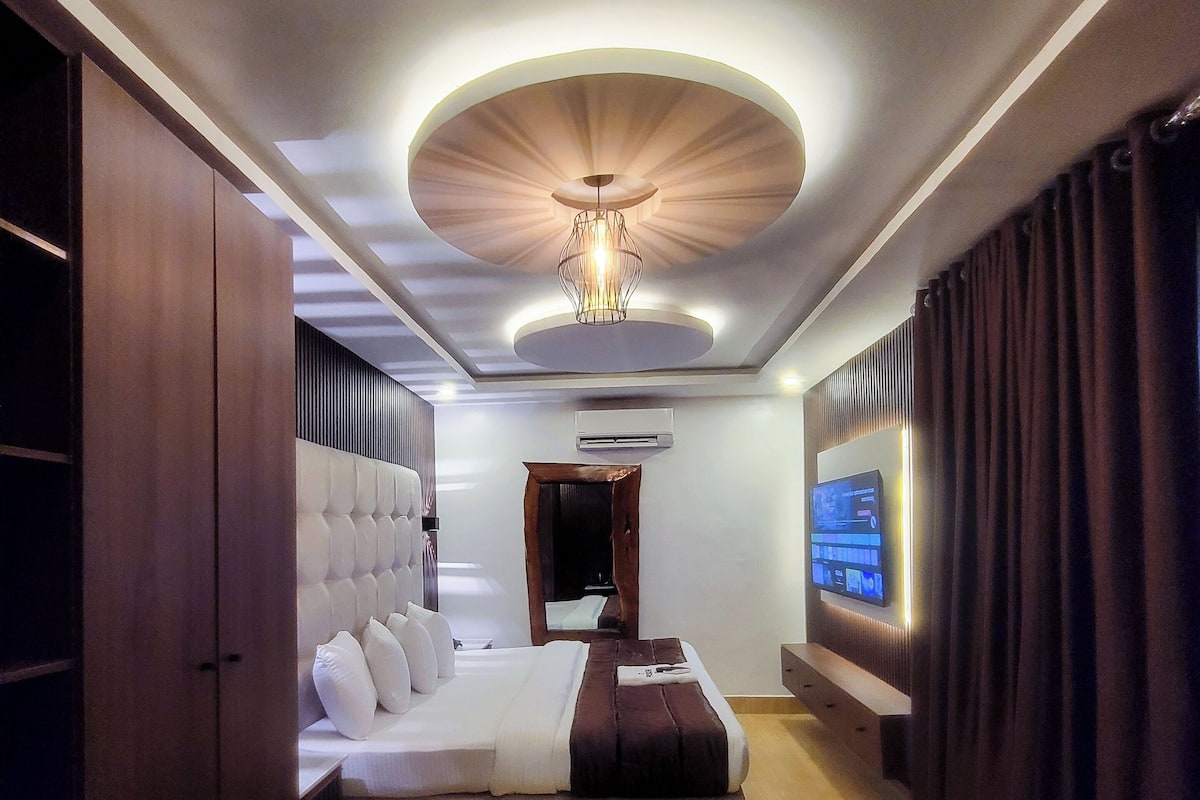 A modern hotel room with a large bed, a television, and a ceiling light fixture.