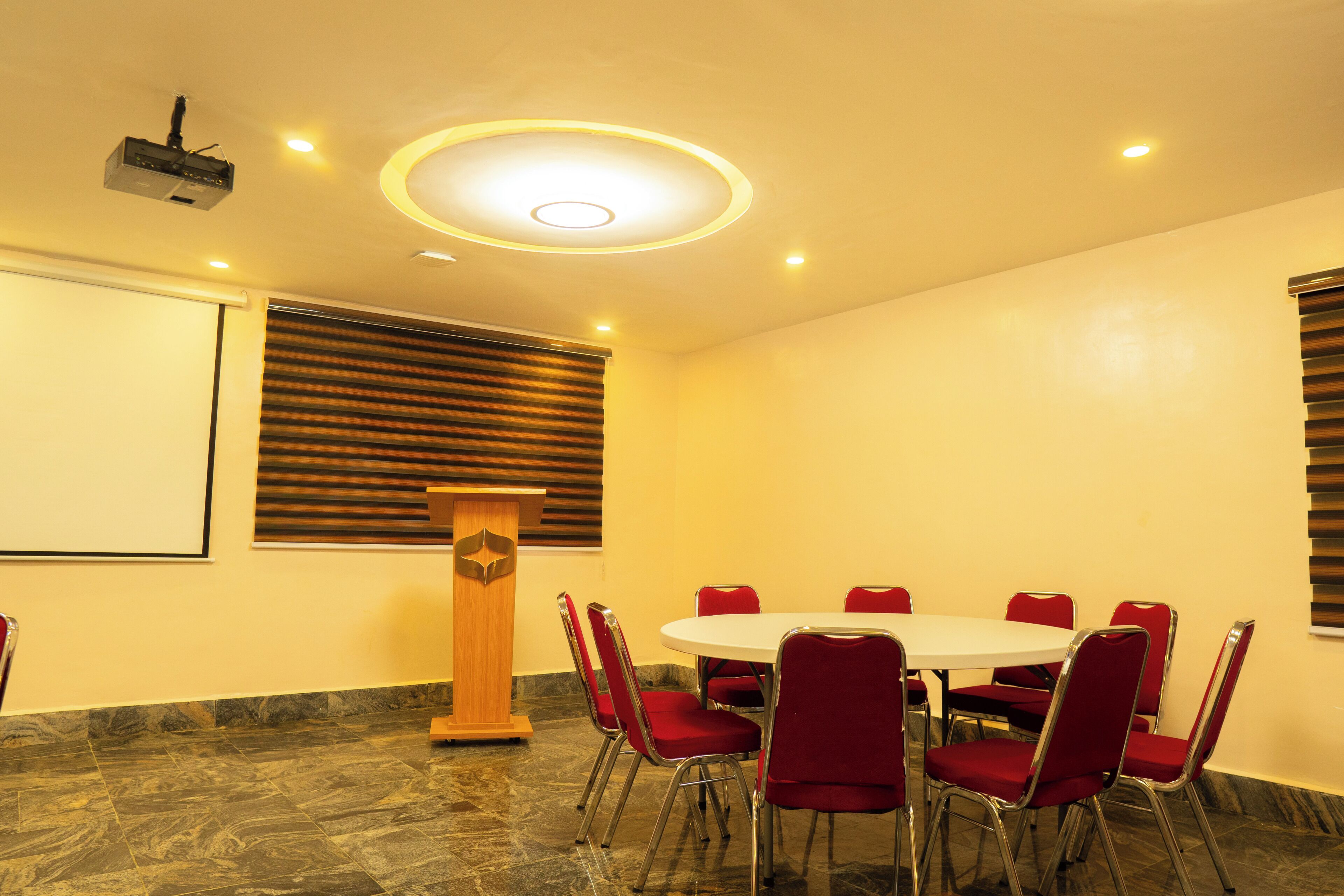 A conference room with a round table, red chairs, a podium, and a projector.
