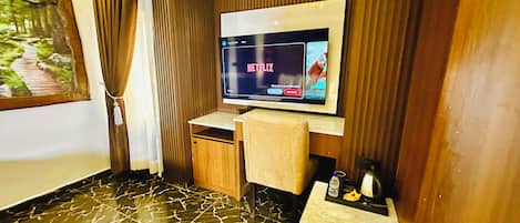 A hotel room with a flat-screen TV mounted on the wall, a wooden cabinet, a small table, and a marble-patterned floor.