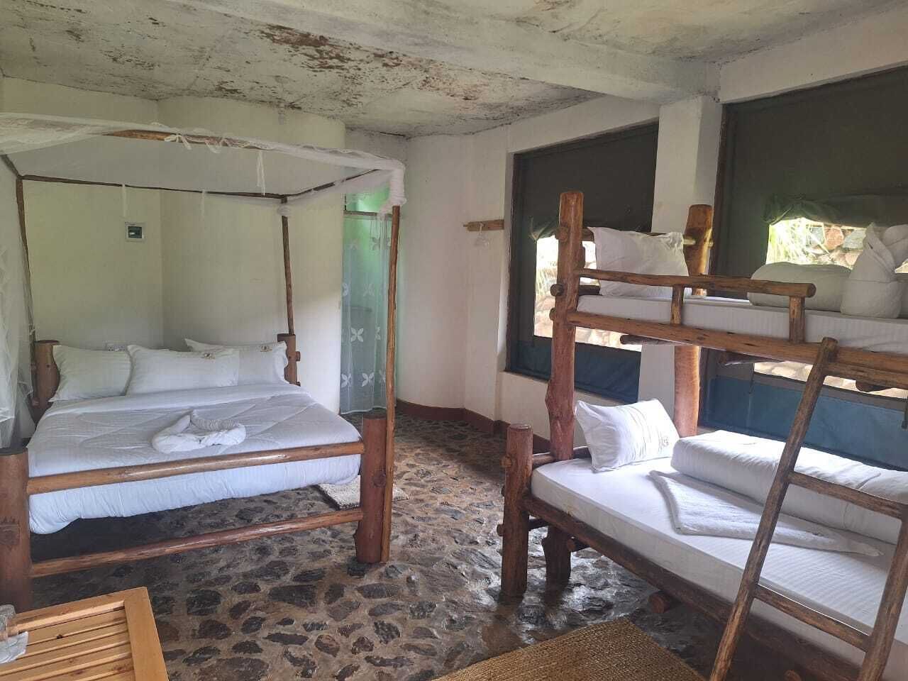 A rustic room with two wooden beds, one with a canopy and one without, a stone floor, and a window with a view.