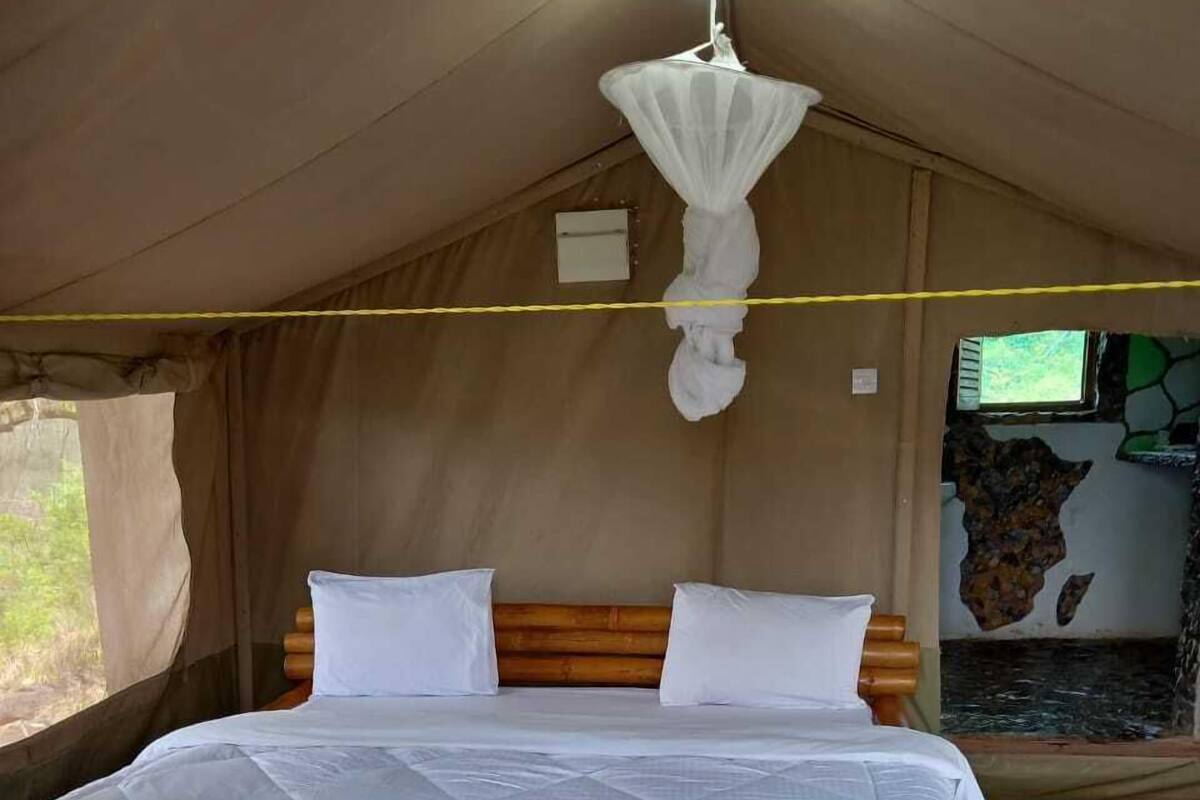 A tented room with a bed, a hanging mosquito net, and a stone wall with a window.