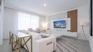 A modern living room with a glass coffee table, white sofas, a flat-screen TV mounted on the wall, and a floor lamp. - 4342 - Great Family Home near Disney, Pool & Spa - Storey Lake Resort (Kissimmee)
