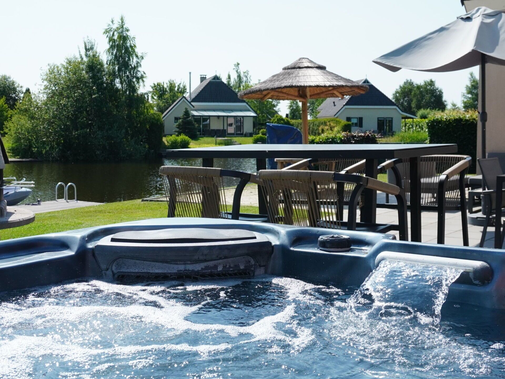 A hot tub with a view of a lake, outdoor furniture, and a house in the background.