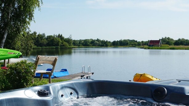 Ein Boot mit einer Bugwelle, ein Steg und ein See mit einem Haus im Hintergrund.