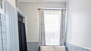 Une chambre à coucher avec un lit, une fenêtre avec des rideaux, un ventilateur de plafond et une armoire.