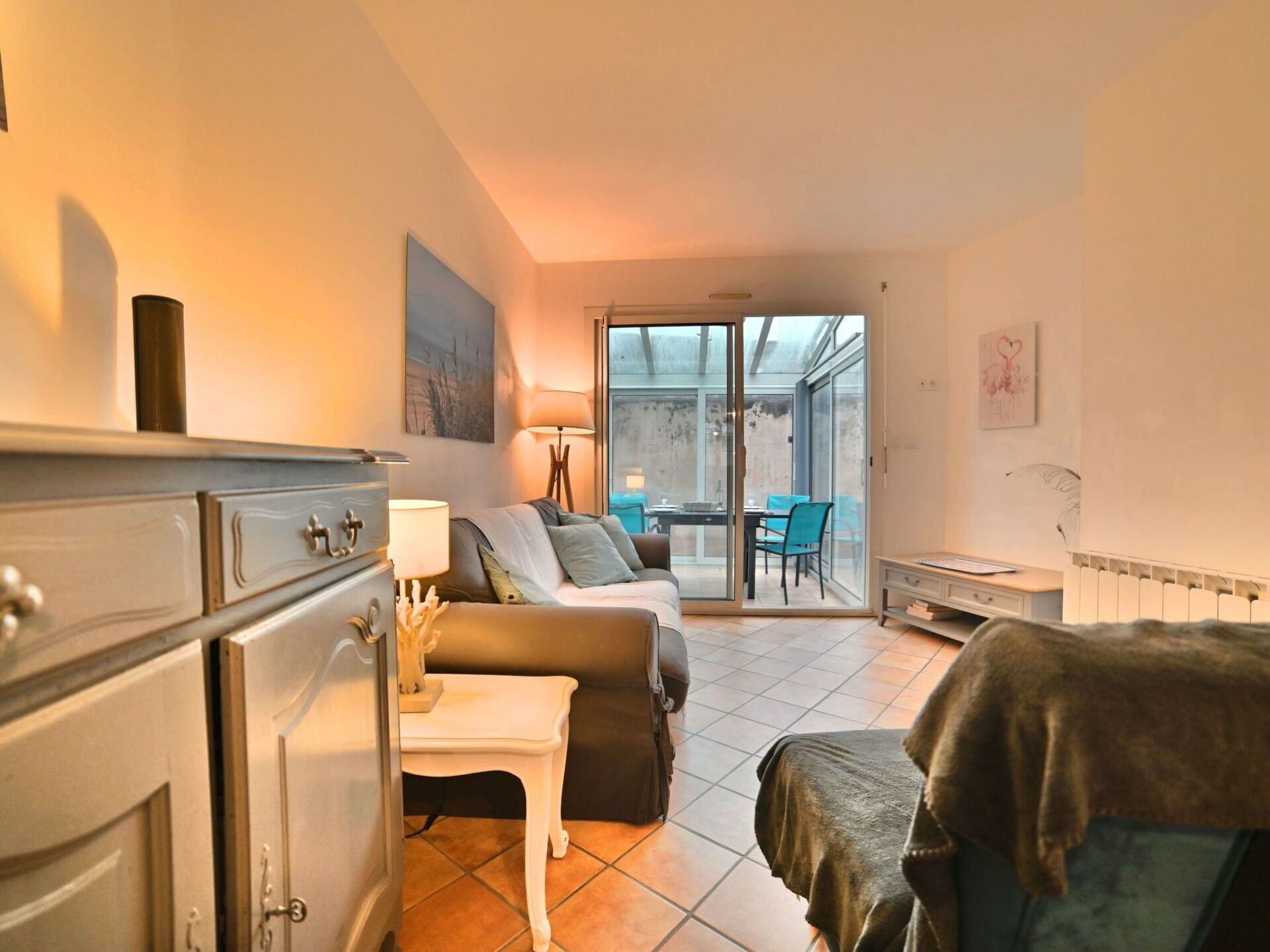 Un salon confortable avec un canapé, une petite table et un fauteuil. Une porte-fenêtre coulissante donne accès à un balcon aménagé avec des sièges d’extérieur.